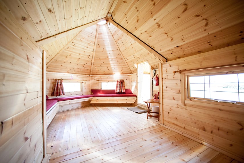 Interior of a camping cabin at Ernests Retreat. The cabin benches have red cushions and red tartan curtains are hanging above the windows.