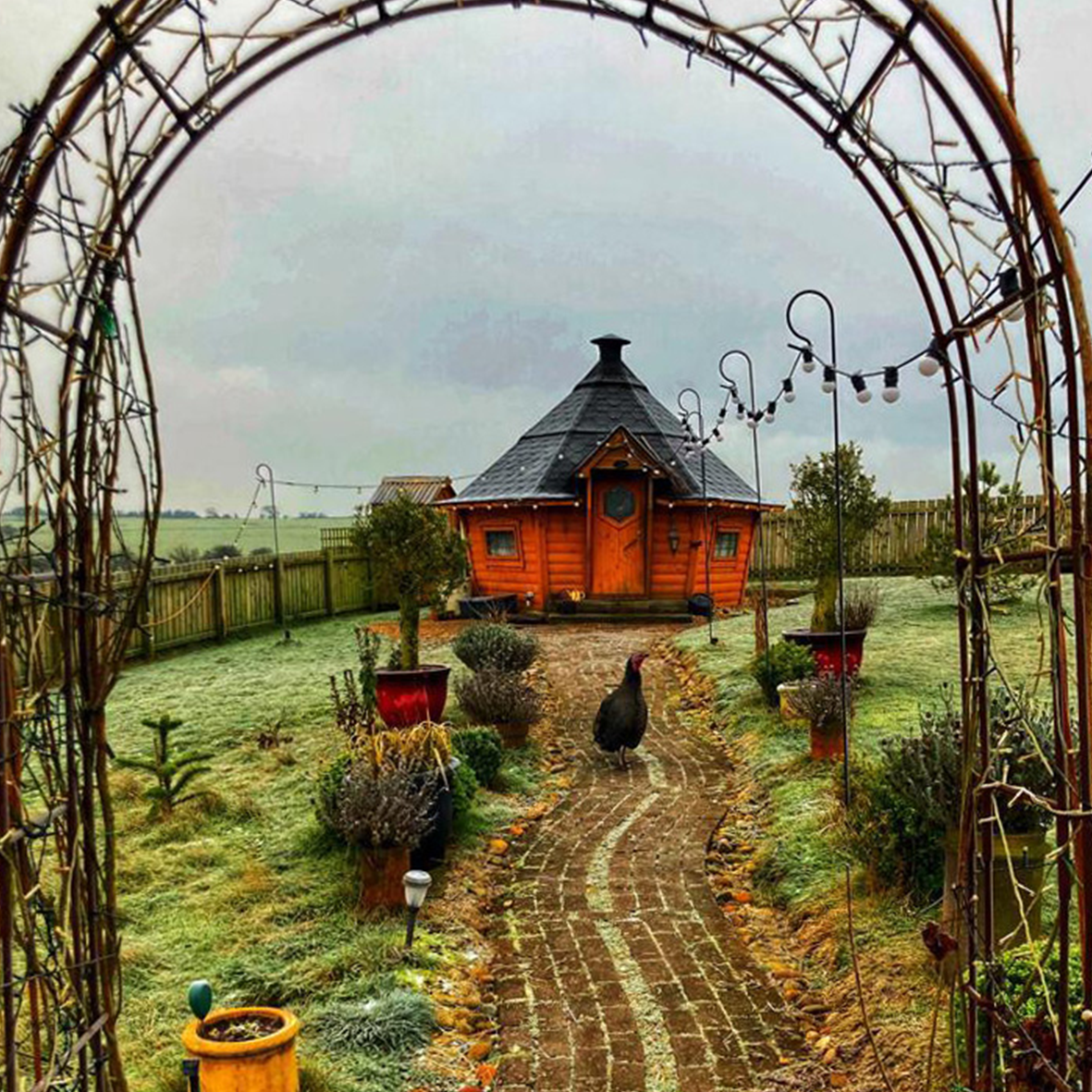 The exterior of the Hungry Obbit BBQ hut. There is a brick path leading to the cabin and a turkey is stood in the middle of the path.
