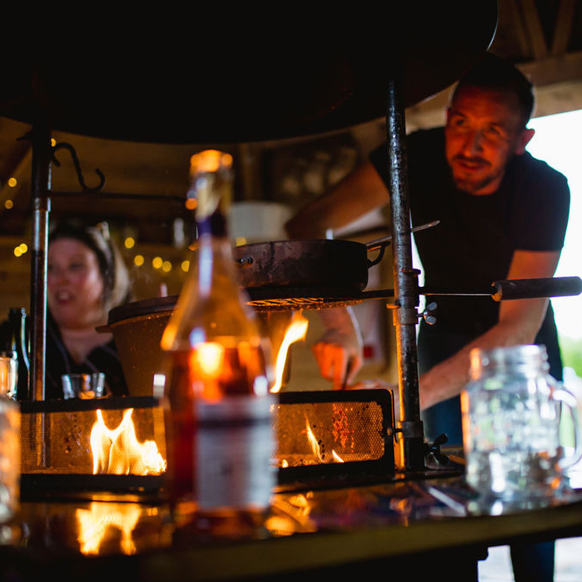 A man cooking for guests on the central grill in a BBQ cabin