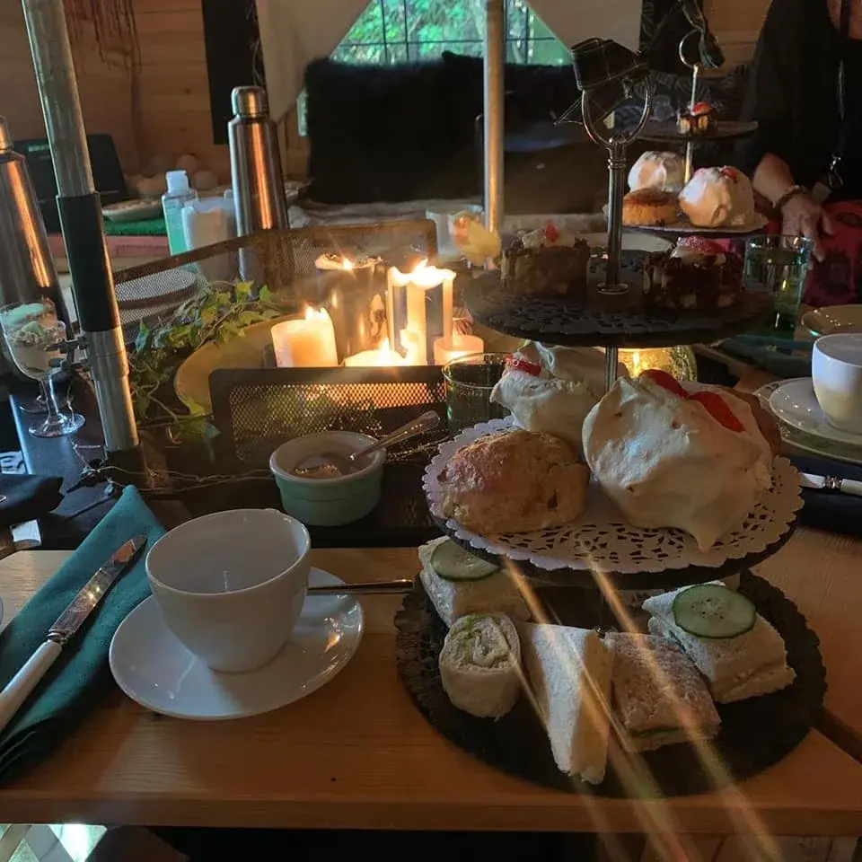 An afternoon tea spread inside a BBQ cabin. There are candles lit in the fire pit to provide soft, cosy lighting.